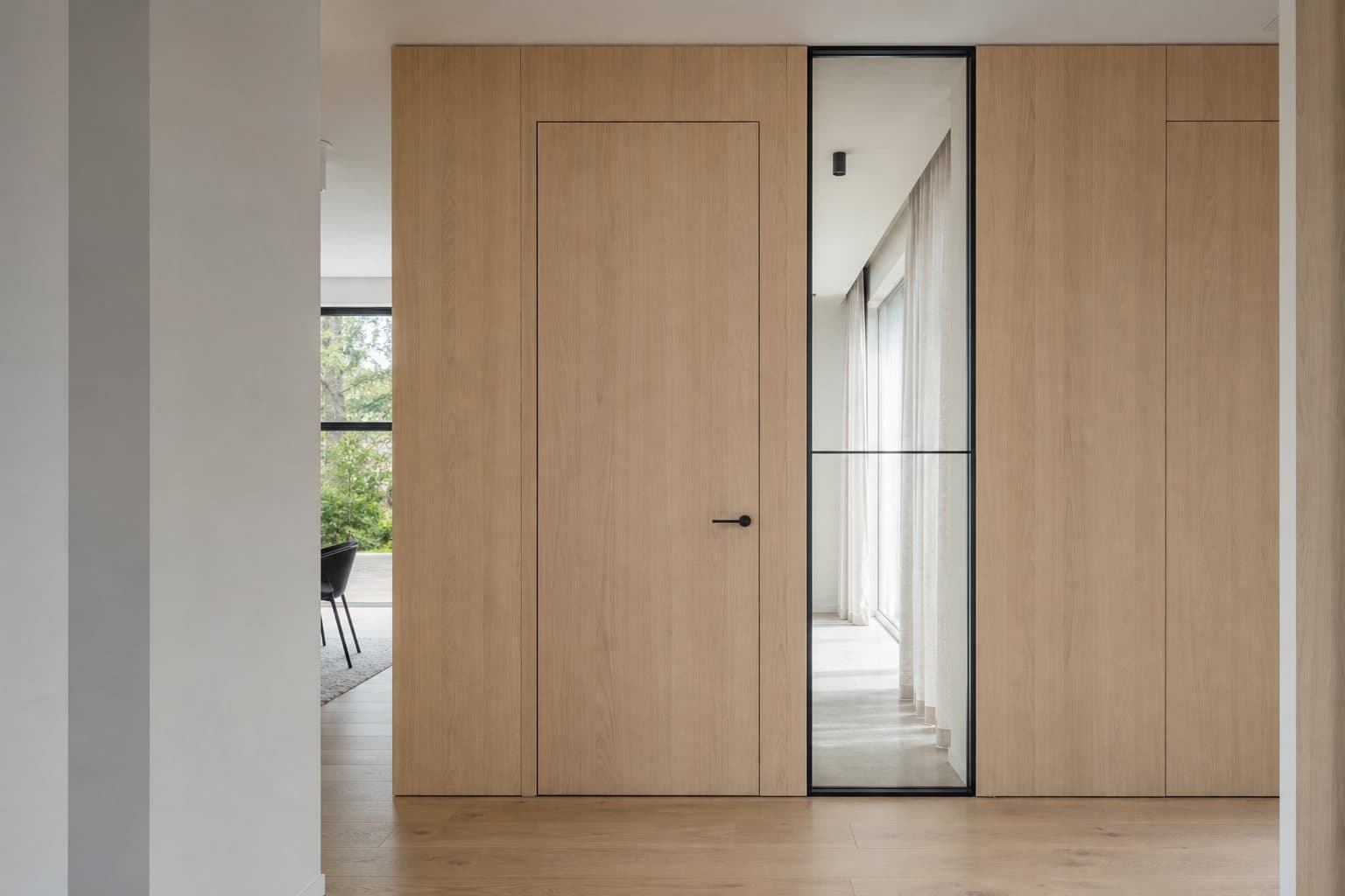 Full-height flush oak interior door integrated with wall paneling and a glazed partition