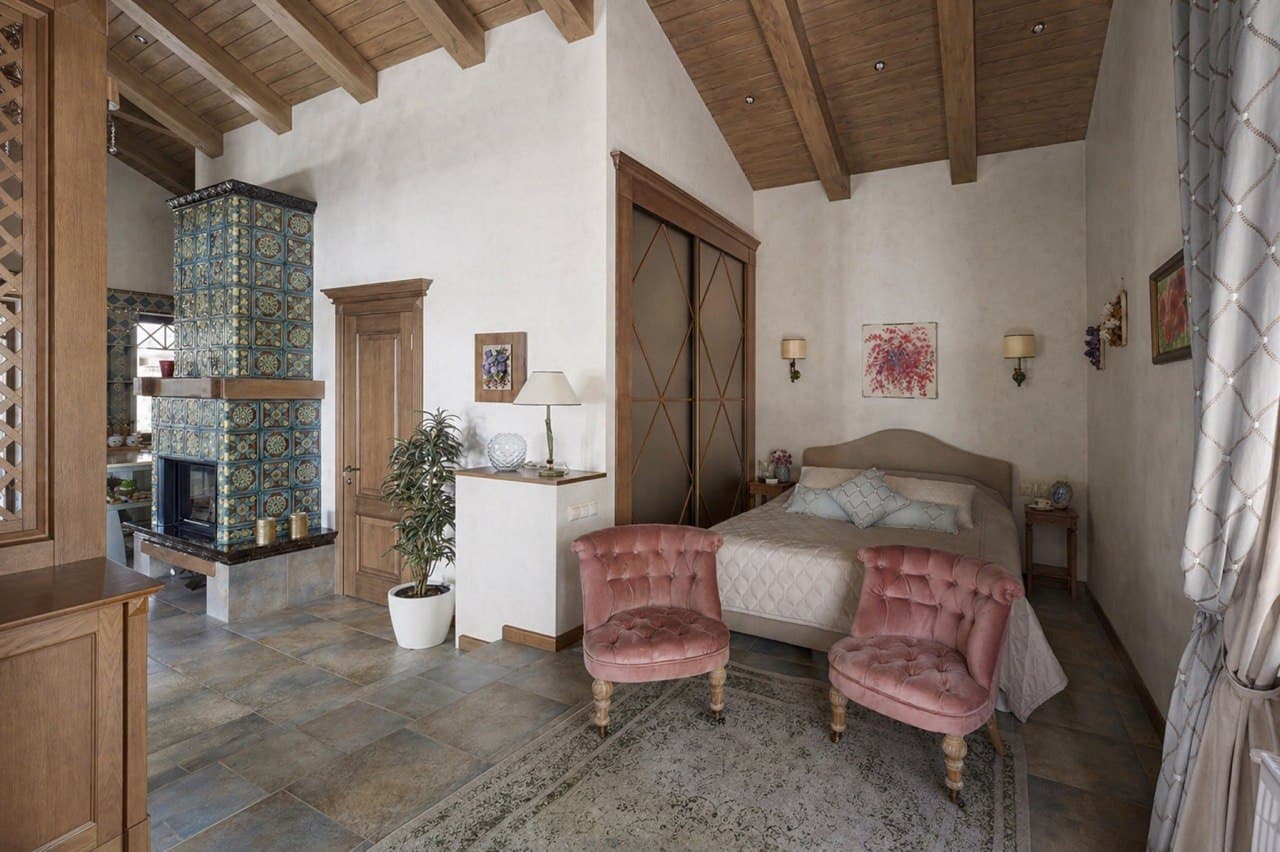 Bedroom with decorative plaster walls, a tiled stove, and pink armchairs