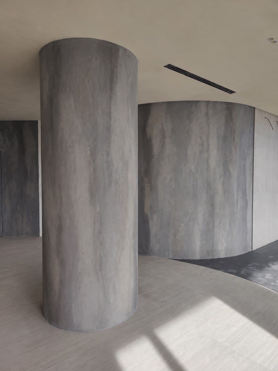 Cylindrical column with mineral texture and a curved architectural wall