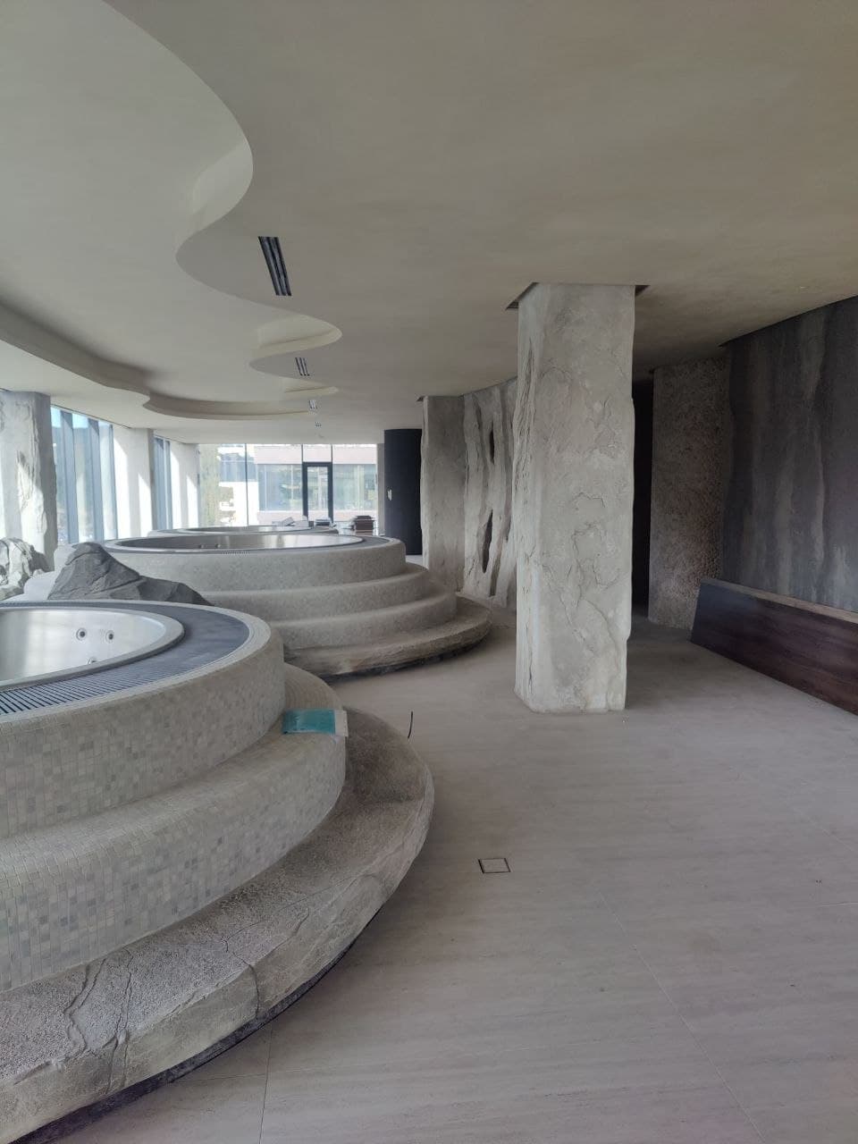 Sculptural lounge with curved platforms, textured columns, and panoramic glazing