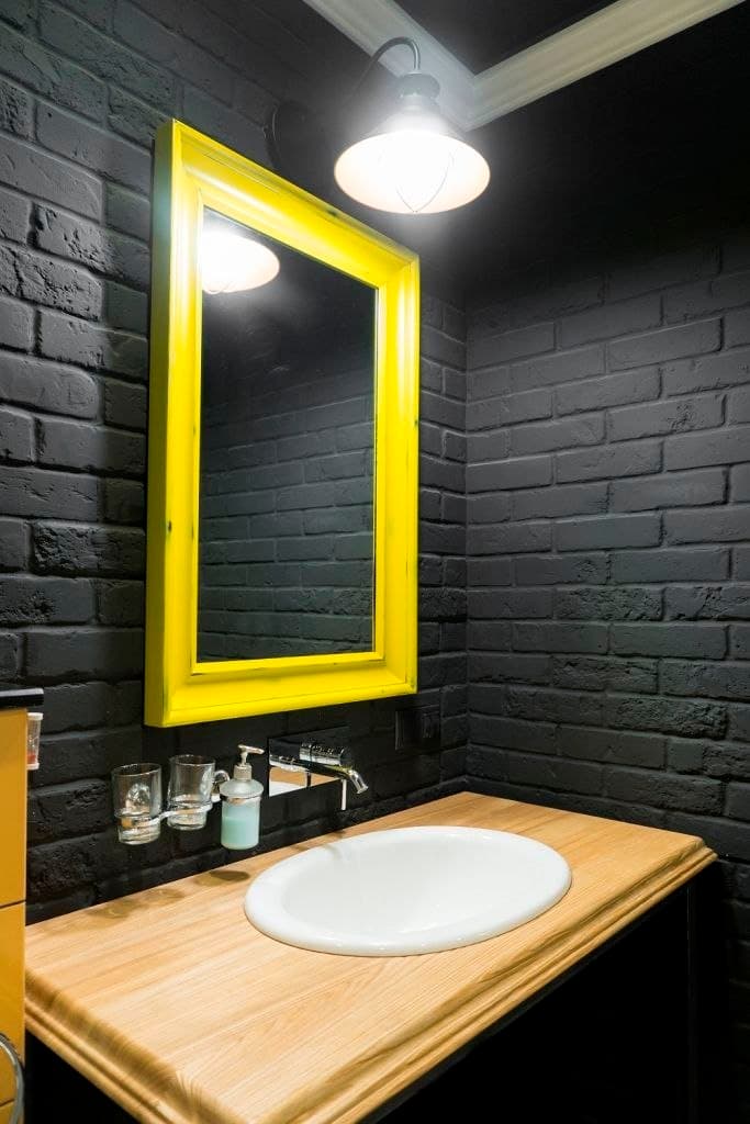 Powder room with black brick walls, a yellow mirror, and a wood countertop