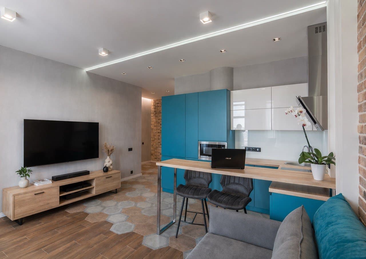 Open-plan living room with a turquoise kitchen, decorative plaster, and a brick accent wall