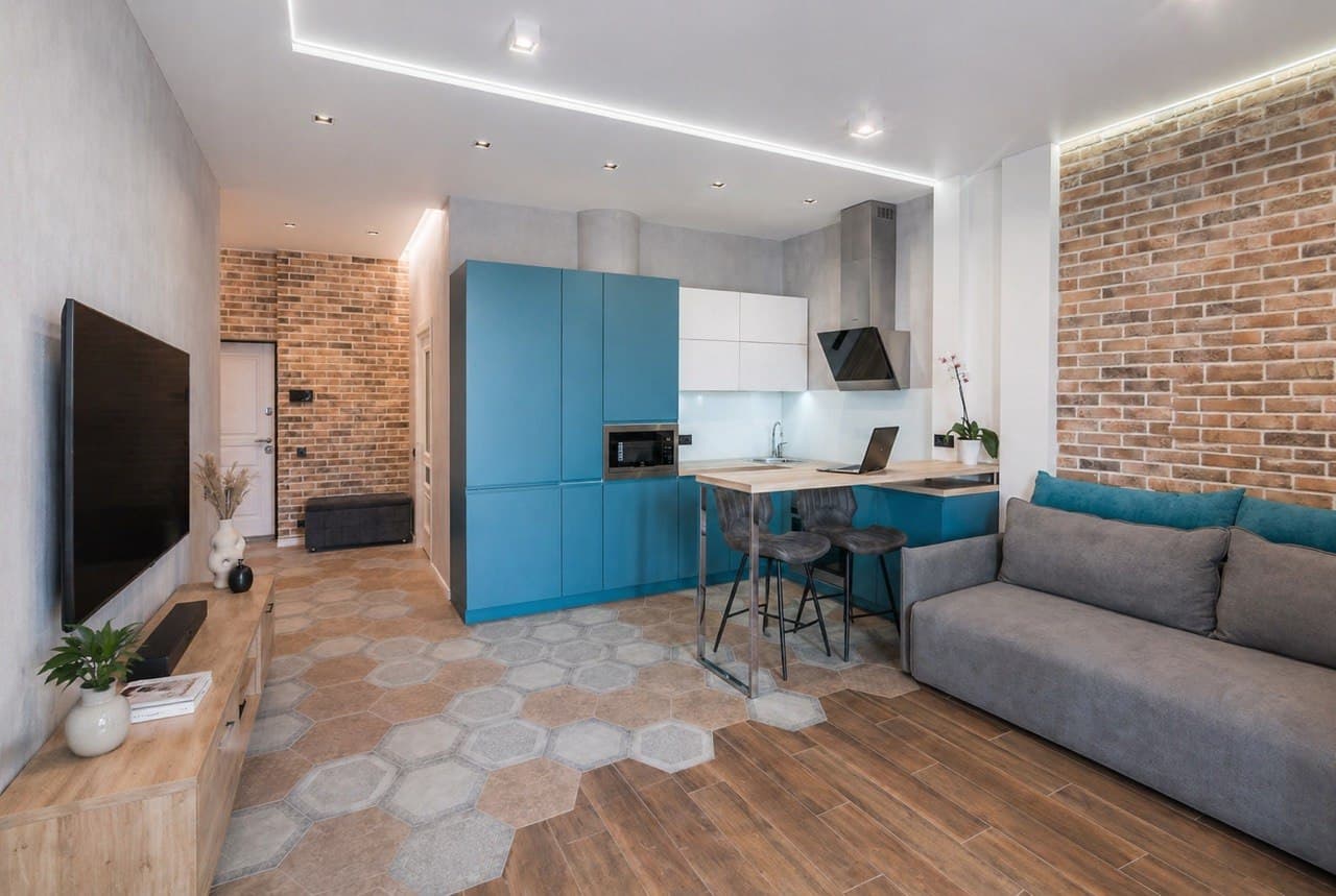 Studio kitchen and lounge with textured floors, a brick wall, and blue cabinetry