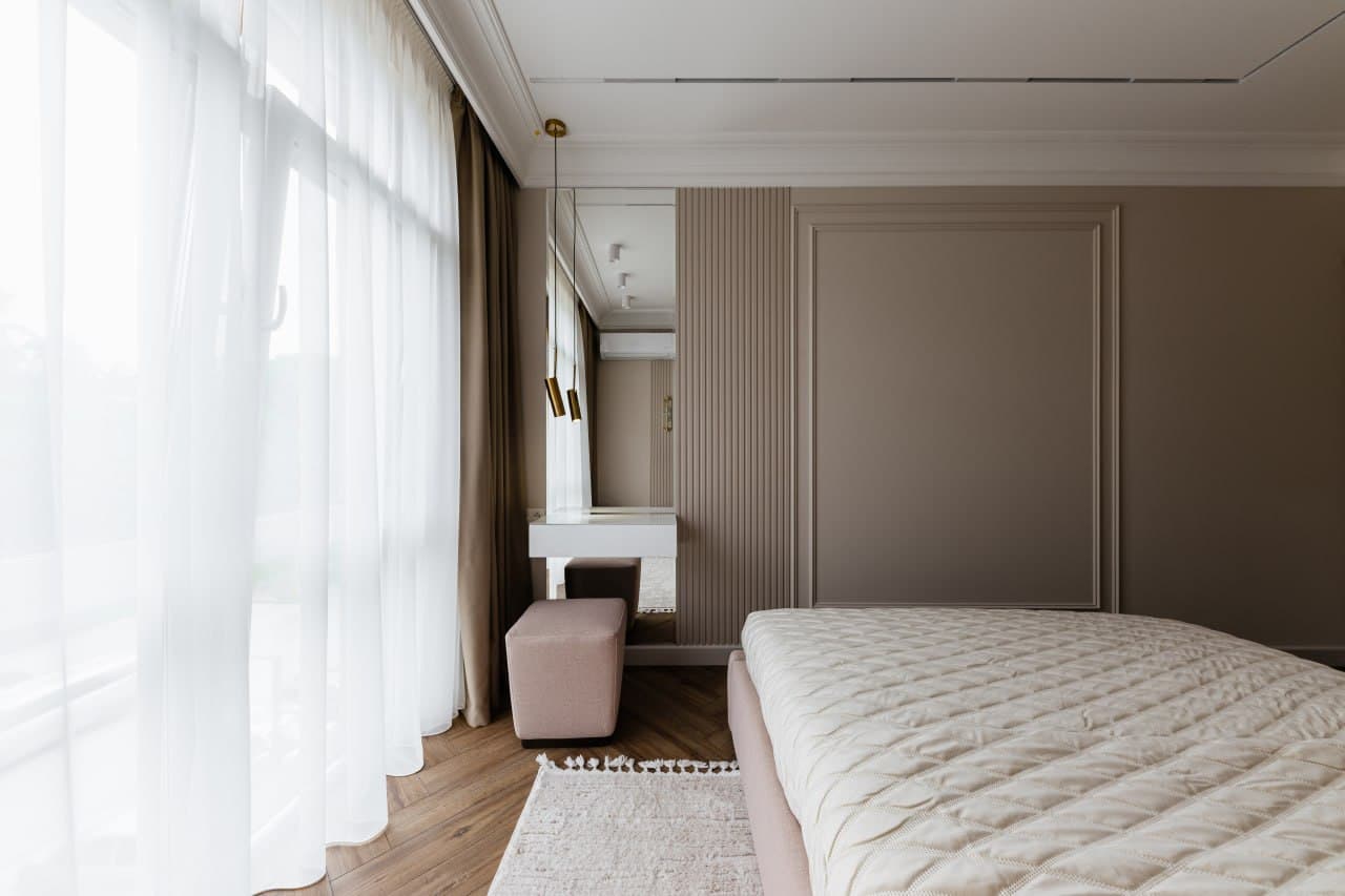 Bedroom corner with sheer curtains, paneled walls, and a minimal dressing table