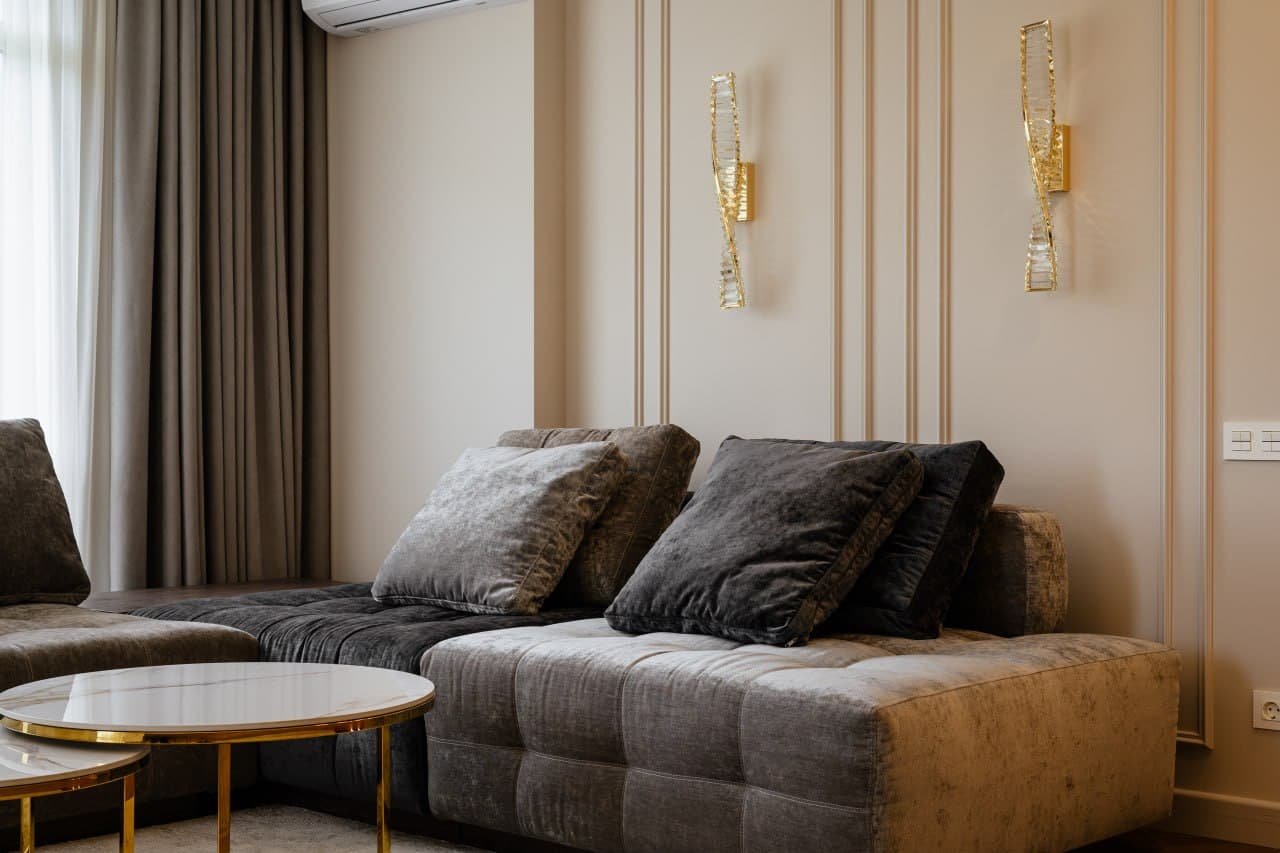 Sofa corner with decorative wall panels, brass sconces, and layered curtains