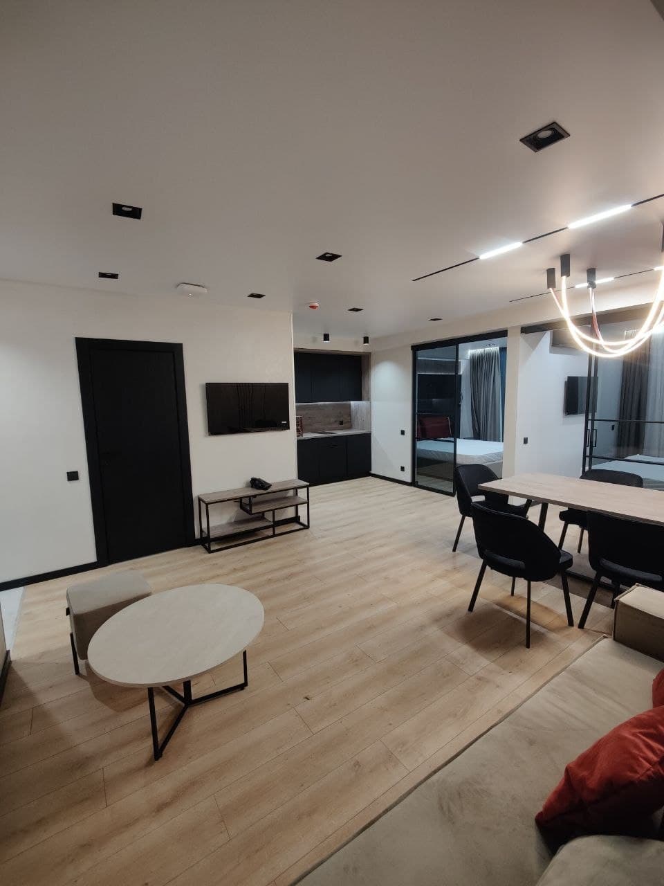 Open-plan living room with minimal furniture, white walls, and a chandelier