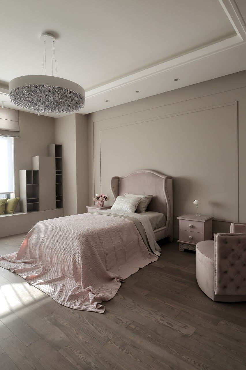 Bedroom with a soft curved headboard, matte decorative walls, and a pendant chandelier