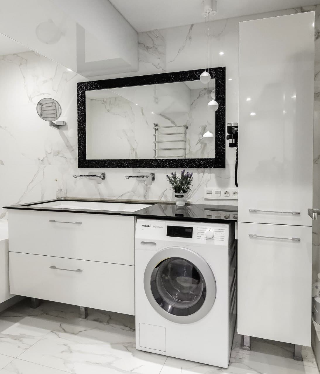 Compact bathroom with marble-look tiles, a black mirror frame, and a laundry zone