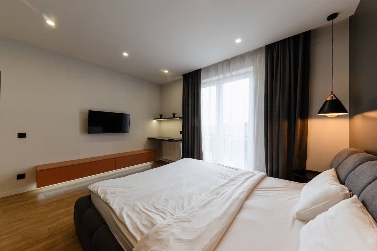 Studio bedroom with a floating media shelf, curtain wall, and warm wood accents